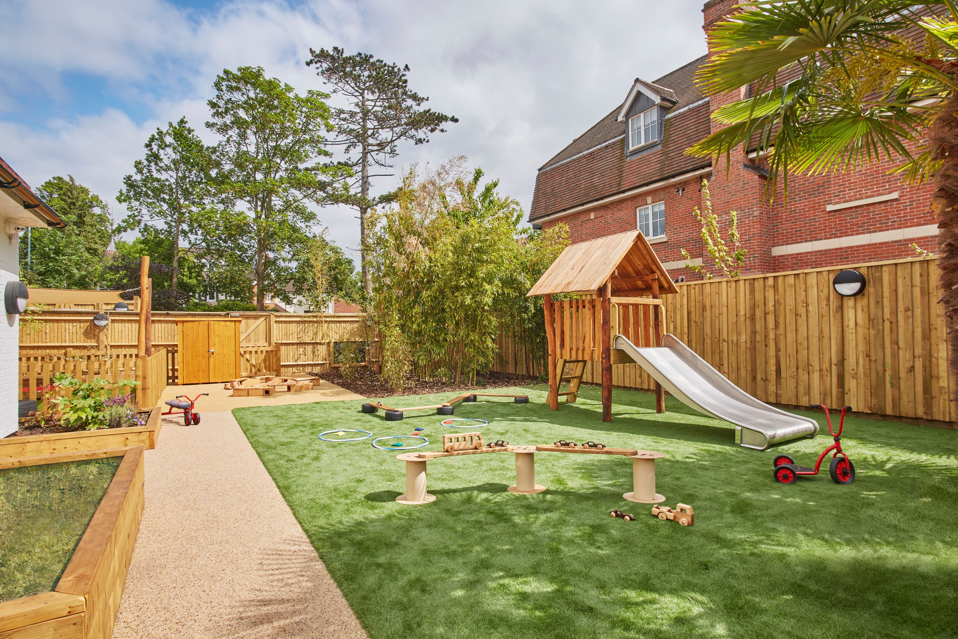 A well-maintained outdoor children's playground with artificial grass, a wooden play structure with a slide, and a paved path.