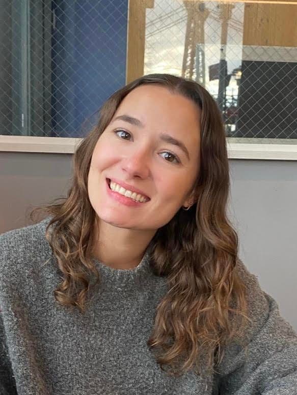 Smiling woman with wavy brown hair wearing a grey sweater.