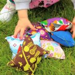 A little girl picking up colourful beanbags from grass