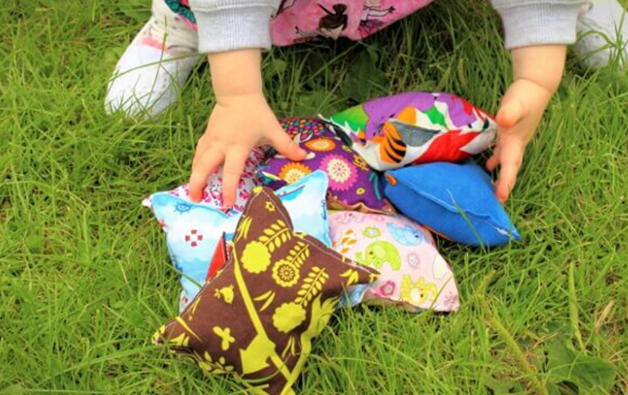 A little girl picking up colourful beanbags from grass