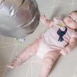 A little baby laying on the bed and looking up at a balloon