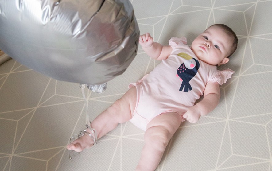 A little baby laying on the bed and looking up at a balloon