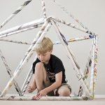 A little boy sitting in a newspaper sculpture