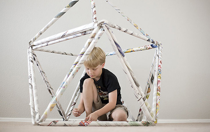 A little boy sitting in a newspaper sculpture