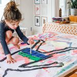 A girl painting an outline of a person on a canvas - body tracing