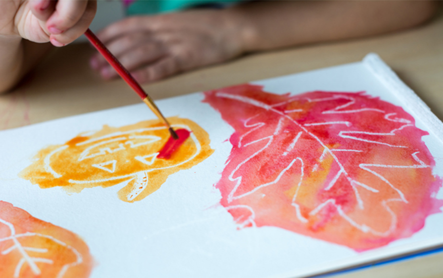 A white crayon drawing of a leaf and pumpkin