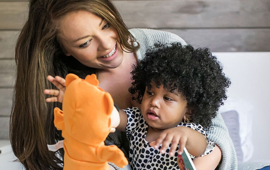 A woman holding her daughter while she reaches for a toy