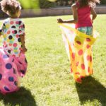 Two children in colourful sacks in a sack race across a lawn