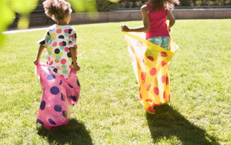 Two children in colourful sacks in a sack race across a lawn