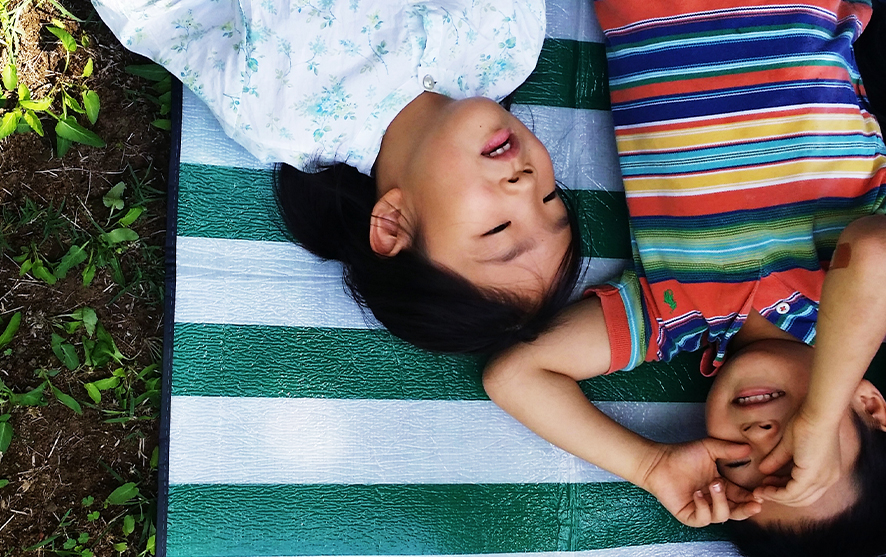 Two children laying on the ground and looking at clouds