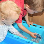 Two children playing with foil boats in a tub