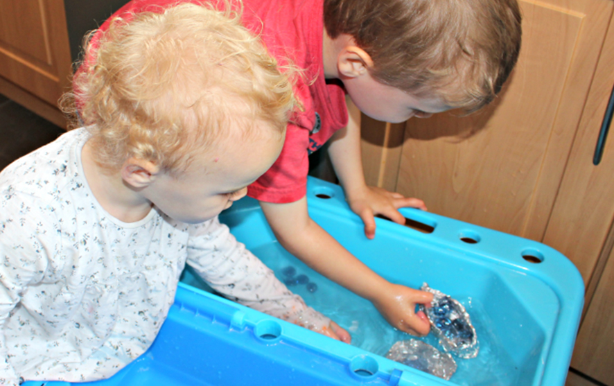 Two children playing with foil boats in a tub