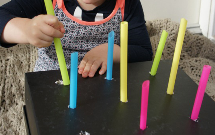 A child playing the push and pull game with straws and cardboard box