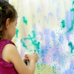 A little girl using a spray bottle to water paint