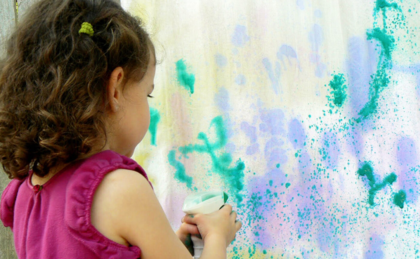 A girl using a spray bottle with paint to make art