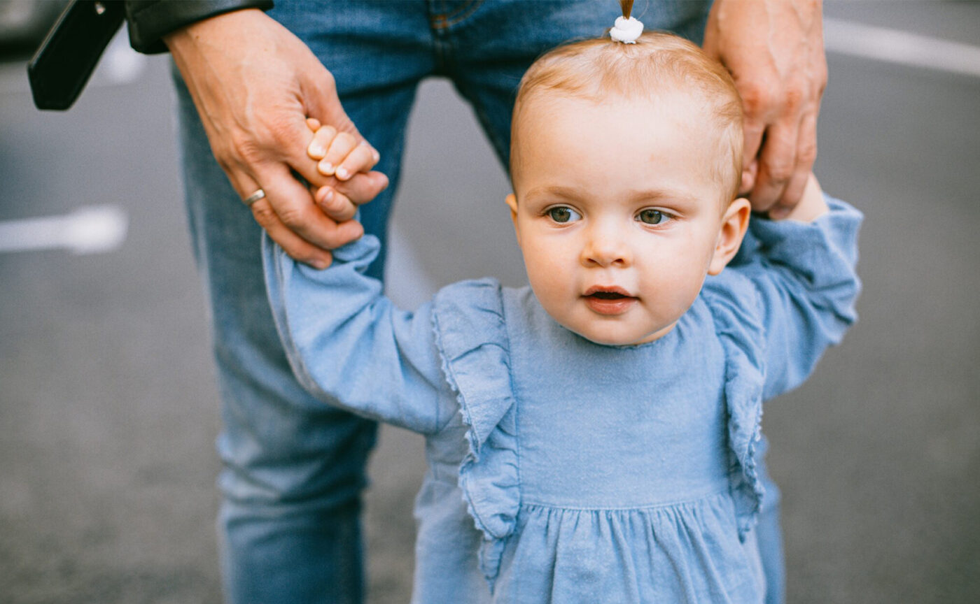 A dad holding a small child by the hands as they learn to walk