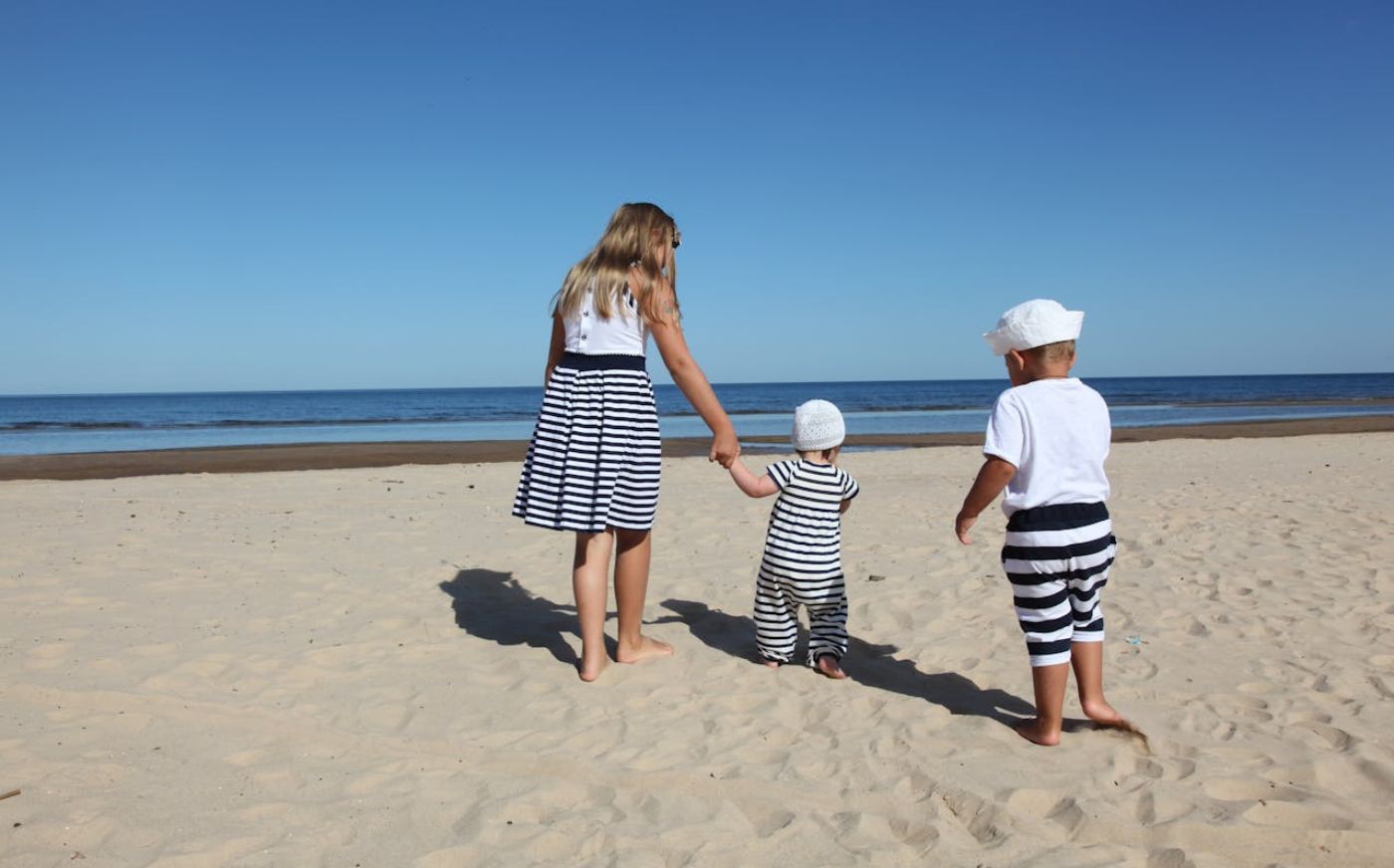 three kids on a sandy beach looking at the sea - family holiday