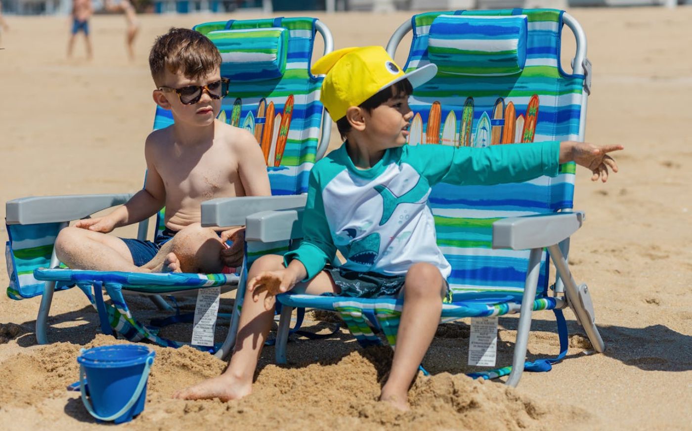 Two boys sitting on beach chairs on a sandy beach