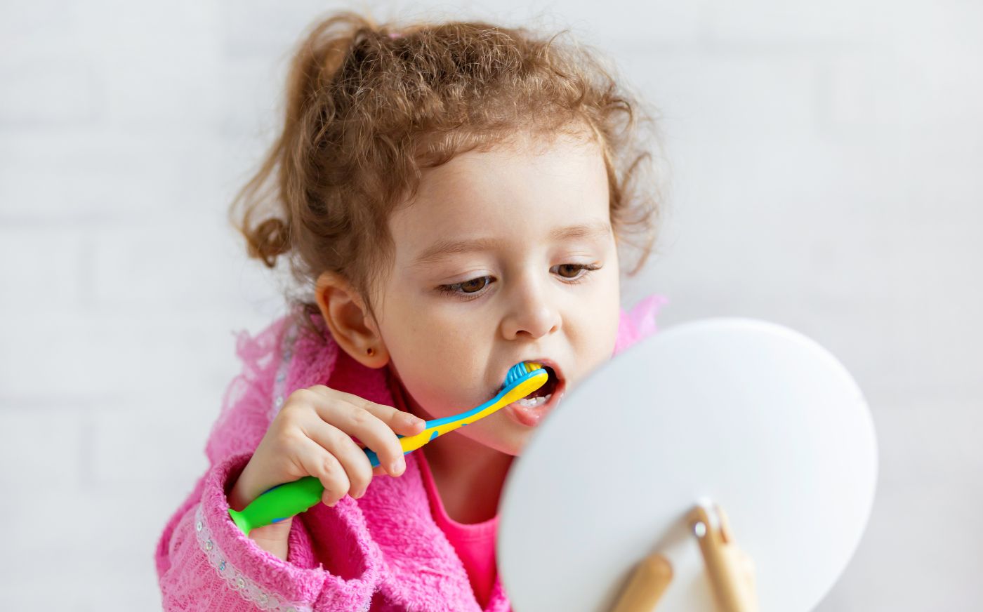 A little girl looking in the mirror and brushing her teeth