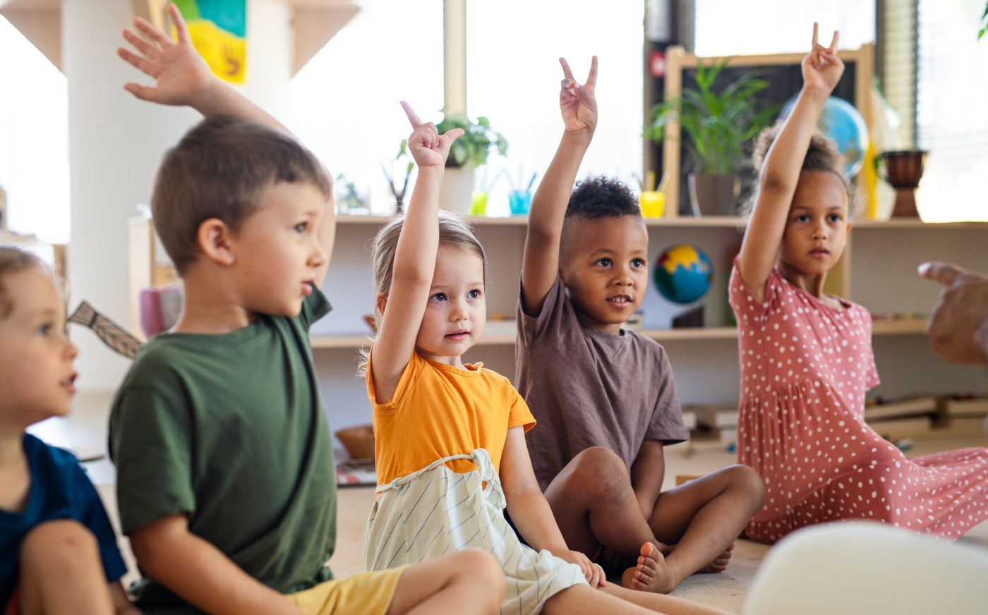 Children sitting on the floor in school raising their hands