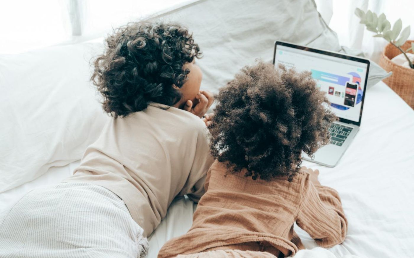 Two children laying on the bed looking at something on a laptop