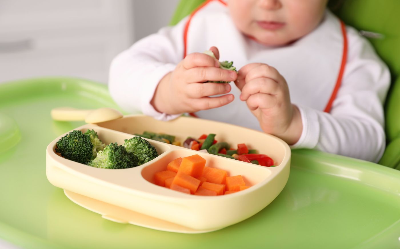 A baby in a highchair with a plate of veggies in front of it