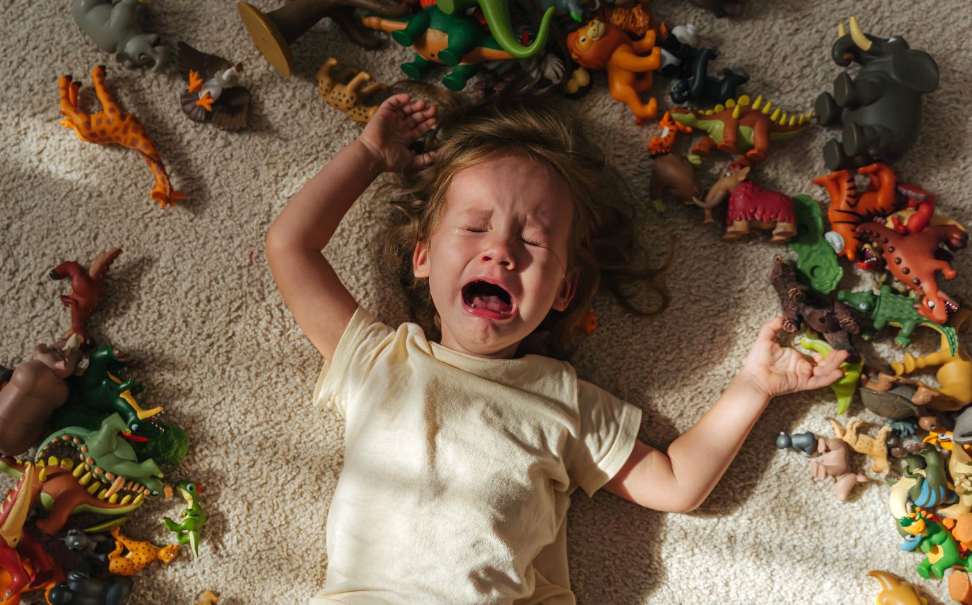 A toddler crying and lying on the floor surrounded by toys, throwing a tantrum. Challenging behaviours in children